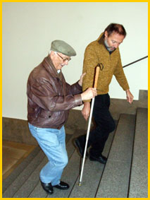 Bild: Michael Kleiss zeigt einem Späterblindeten im Seniorenalter den Gebrauch des Blindenlangstocks beim treppensteigen